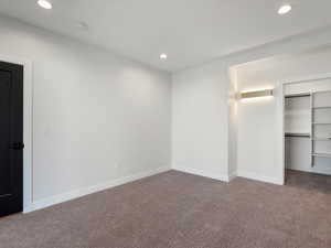 Unfurnished bedroom featuring a walk in closet, recessed lighting, and dark carpet