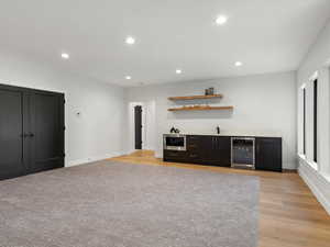 Indoor wet bar with dark cabinets, open shelves, recessed lighting, wine cooler, and stainless steel microwave