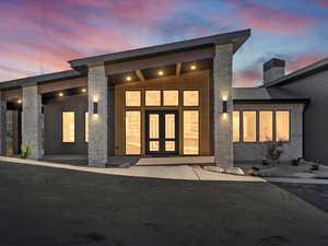 Exterior entry at dusk with stone siding, a chimney, and french doors
