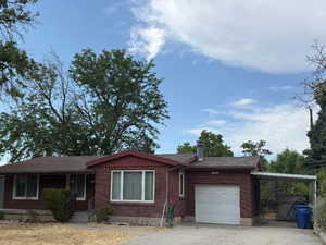 Ranch-style house featuring brick siding, driveway, a chimney, an attached garage, and a carport