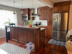 Kitchen with appliances with stainless steel finishes, wall chimney exhaust hood, pendant lighting, and dark wood-style floors