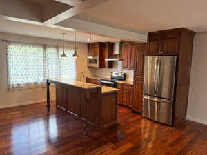 Kitchen featuring appliances with stainless steel finishes, pendant lighting, light stone countertops, wall chimney exhaust hood, and a kitchen island with sink