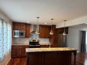 Kitchen with stainless steel appliances, backsplash, light stone countertops, wall chimney exhaust hood, and recessed lighting