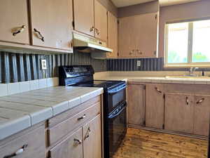 Kitchen with double oven range, tile countertops, under cabinet range hood, and dark wood-type flooring