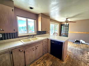 Kitchen with a peninsula, dishwasher, dark wood-style flooring, and tile counters