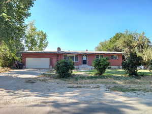 Ranch-style home featuring dirt driveway, brick siding, an attached garage, and a chimney
