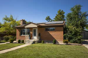 View of front of house featuring a chimney, solar panels, a front lawn, and brick siding