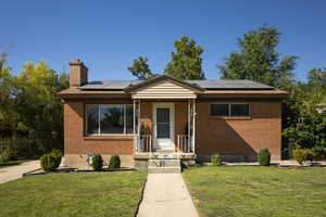 View of front of home with a front yard, a chimney, brick siding, and solar panels