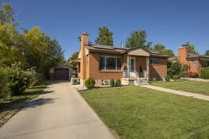 View of front of home with a front yard, an outdoor structure, a chimney, brick siding, and a detached garage