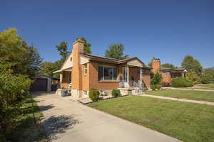 Ranch-style house with an outdoor structure, a chimney, a detached garage, a front lawn, and brick siding