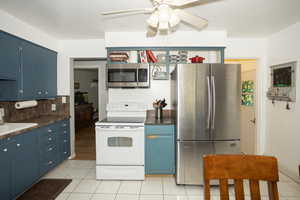 Kitchen featuring blue cabinets, dark countertops, stainless steel appliances, and light tile patterned floors