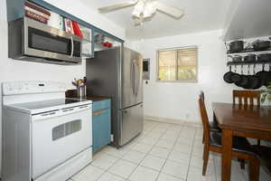 Kitchen with stainless steel appliances, blue cabinets, dark countertops, light tile patterned flooring, and ceiling fan