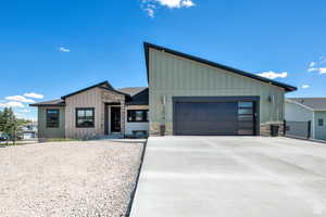 View of front of property featuring board and batten siding, stone siding, a garage, and concrete driveway