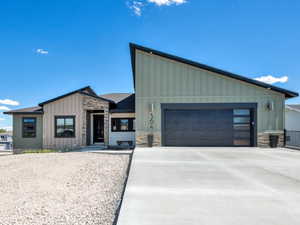 View of front of property featuring board and batten siding, stone siding, a garage, and concrete driveway