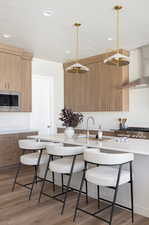 Kitchen with light wood finished floors, pendant lighting, wall chimney range hood, a breakfast bar, and recessed lighting
