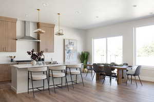 Kitchen with wall chimney exhaust hood, a kitchen bar, light stone countertops, light wood finished floors, and hanging light fixtures