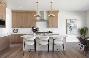 Kitchen featuring wood finished floors, wall chimney exhaust hood, a breakfast bar, recessed lighting, and decorative light fixtures