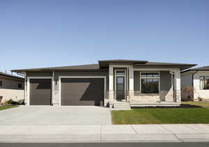 Prairie-style house with driveway, stone siding, a garage, and covered porch