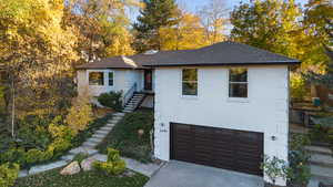View of front facade featuring brick siding, a shingled roof, driveway, stairway, and a garage