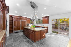 Kitchen with light stone countertops, open shelves, recessed lighting, an island with sink, and paneled built in fridge
