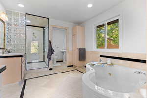 Bathroom featuring inlaid floor details, vanity, tile walls, a tub with jets, and a stall shower
