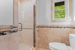 Full bath featuring tile walls, a wainscoted wall, and a shower stall