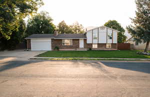 Split level home with brick siding, a garage, concrete driveway, and a chimney