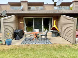 Rear view of house featuring brick siding, a patio, roof with shingles, and a lawn