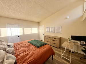 Bedroom with vaulted ceiling, wood finished floors, an office area, and a textured ceiling