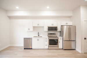 Kitchen featuring stainless steel appliances, white cabinets, recessed lighting, and light wood finished floors
