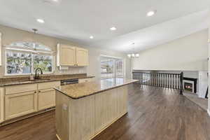 Kitchen featuring light brown cabinetry, hanging light fixtures, light stone countertops, a center island, and lofted ceiling