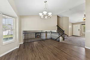 Empty room featuring stairway, lofted ceiling, dark wood-style flooring, a chandelier, and a ceiling fan