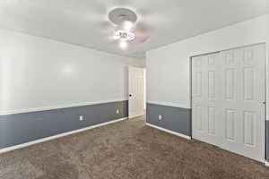 Unfurnished bedroom featuring attic access, dark carpet, a closet, and a ceiling fan