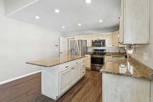 Kitchen featuring stainless steel appliances, recessed lighting, dark wood-type flooring, dark stone countertops, and a center island