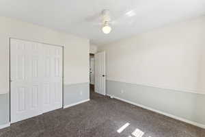 Unfurnished bedroom featuring dark carpet, a closet, and ceiling fan