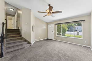 Carpeted entrance foyer with vaulted ceiling, ceiling fan, and stairway