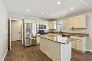 Kitchen featuring stainless steel appliances, light stone countertops, light brown cabinetry, a center island, and recessed lighting