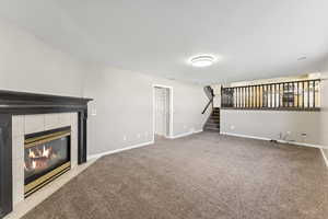 Unfurnished living room featuring a tile fireplace, light colored carpet, and stairway