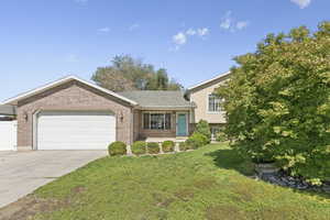 Tri-level home featuring driveway, a garage, a front yard, and brick siding