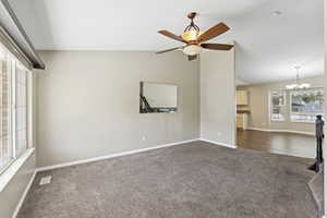 Unfurnished living room with dark colored carpet, lofted ceiling, a chandelier, and a ceiling fan