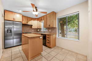 Kitchen with a kitchen island, stainless steel refrigerator with ice dispenser, backsplash, light tile patterned floors, and a textured ceiling