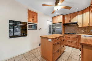 Kitchen featuring wood counters, backsplash, stainless steel appliances, light tile patterned floors, and a ceiling fan