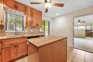 Kitchen with light tile patterned floors, decorative backsplash, ceiling fan, wooden counters, and a kitchen island