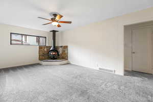 Unfurnished living room with a wood stove, carpet, ceiling fan, and wooden walls