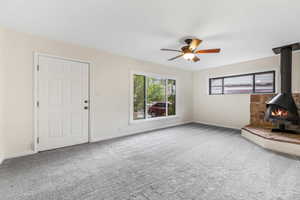 Unfurnished living room with a wood stove, light carpet, and a ceiling fan