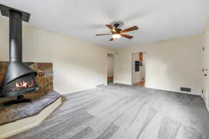 Unfurnished living room with light colored carpet, a wood stove, and a ceiling fan