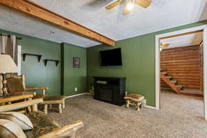 Living area featuring beamed ceiling, carpet flooring, a ceiling fan, a textured ceiling, and stairs