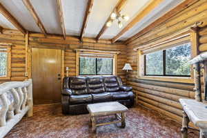 Living room with beam ceiling, carpet floors, and log walls