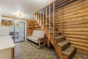 Unfurnished bedroom with log walls, a textured ceiling, carpet floors, freestanding refrigerator, and access to exterior