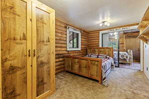 Bedroom with rustic walls, multiple windows, a textured ceiling, and light carpet